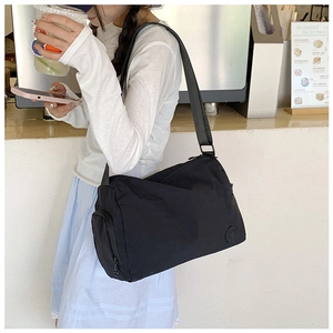 Detail view of a large black nylon crossbody bag with adjustable strap and circular logo