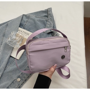 Detailed close-up of a purple nylon crossbody bag with a metallic logo and woven strap