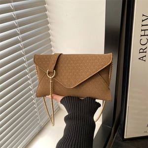 Brown herringbone envelope crossbody bag with gold chain strap in a minimalist setting