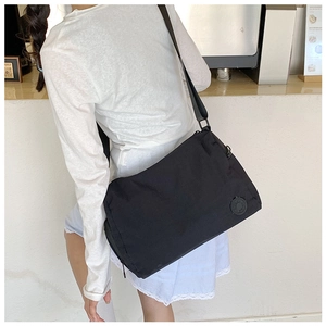 Close-up of large black nylon messenger bag with wide shoulder strap and round logo