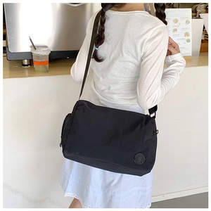 Minimalist black nylon crossbody bucket bag shown in a casual cafe lifestyle setting