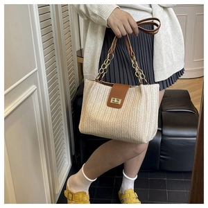 Close-up of beige woven tote bag featuring a leather buckle and gold chain strap detail