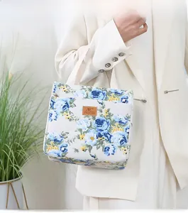 Detail of canvas tote bag with blue and yellow floral print and brown leather logo tag