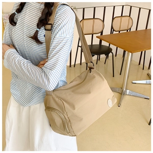 Detail view of a beige nylon bucket bag featuring a zipper side pocket and adjustable strap