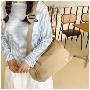Khaki nylon crossbody bucket bag with adjustable strap worn by a model in a cafe