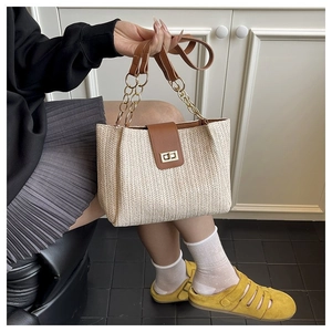 Close-up of beige woven tote bag featuring brown leather flap and gold square twist lock
