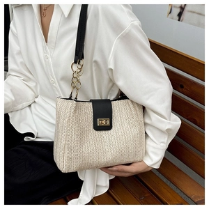 Close-up of woven straw tote bag with black leather strap and gold chain detail