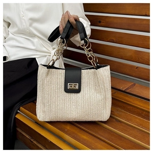 Close-up of beige woven tote bag with black leather flap and golden chain handle detail