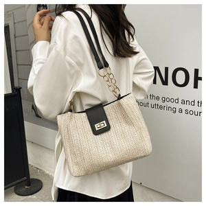 Detail of woven beige tote bag with black leather flap and gold metal twist lock buckle
