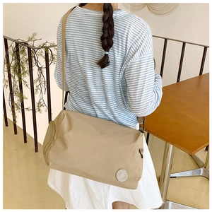 Detail view of beige nylon crossbody bag with adjustable strap and round rubber logo