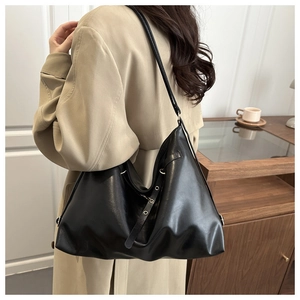 Detail of a black leather hobo bag with silver grommets worn with a khaki trench coat
