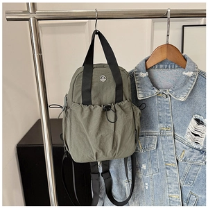 Detail of green nylon travel backpack with drawstring pocket and metal M logo