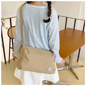 Close-up of beige nylon crossbody bucket bag showing wide strap and circular logo detail