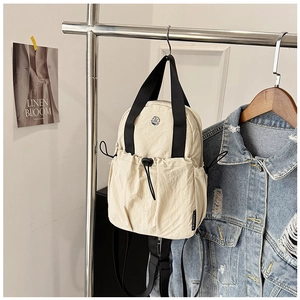 Detail of a cream nylon backpack featuring a drawstring pocket and black handle webbing