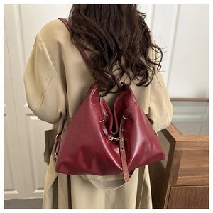 Detail of burgundy oversized shoulder bag in glossy leather worn with a beige coat
