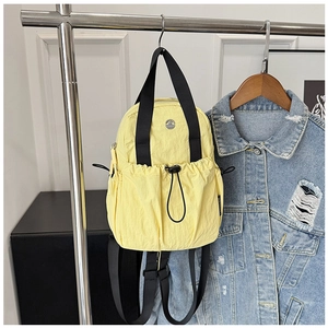 Detail of light yellow mini backpack with black drawstring and brand logo on denim jacket