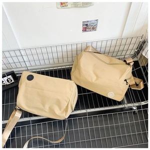 Detail of two khaki nylon cylinder bucket bags with adjustable straps on a metal rack