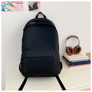 Detail view of a black minimalist backpack on a white desk with campus study accessories