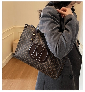 Detail of dark brown tote bag with M letter print and embossed logo on grey blazer
