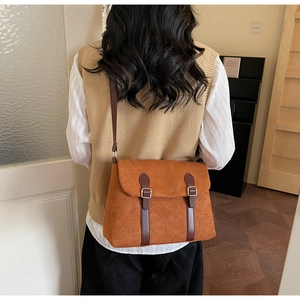 Close-up of a brown suede vintage crossbody bag featuring dark leather straps and silver buckles