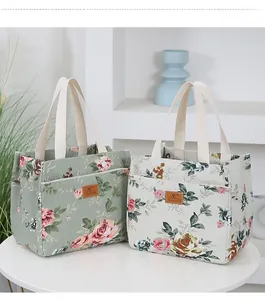 Close-up of bucket lunch bags in sage and cream with pink floral patterns and cotton handles