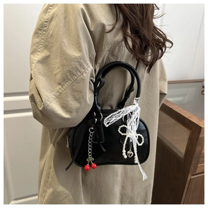 Detail of glossy black bag with lace ribbons, pearl bow charm, and cherry pendant