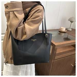 Detail of minimalist black tote bag with gold logo shown on model with brown coat