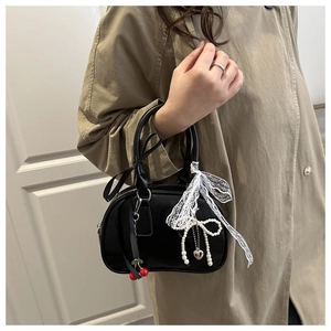 Detail of black Boston bag with cherry charm, white lace bow, and pearl heart pendant