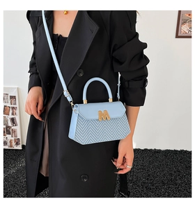 Détail du sac à main bleu clair avec texture tissée, logo M doré et poignée supérieure