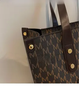Detail of dark brown tote bag with M-pattern print, leather trim and gold rivet studs