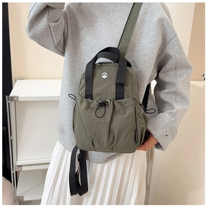 Detail of army green nylon backpack showing metal M logo and side brand tag on model
