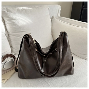 Detail view of large dark brown PU leather tote bag with gold metal eyelets on white sofa