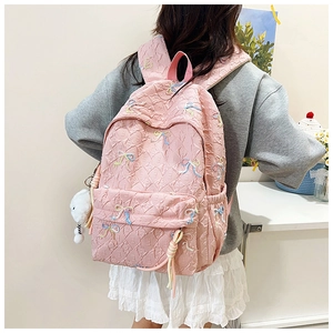 Detail of pink quilted backpack with colorful bow embroidery and a plush pendant