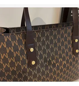 Detail of vintage brown tote bag with M letter pattern and golden rivet hardware