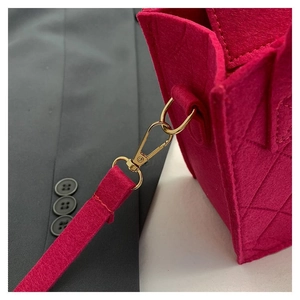 Detaillierte Nahaufnahme der gesteppten Filztasche in Fuchsia mit goldenem Metallkarabiner