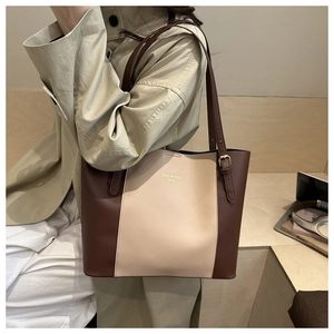 Close-up of beige and brown leather tote bag with adjustable straps and logo print