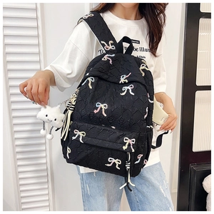 Close-up of black quilted backpack with colorful embroidered bows and plush cloud charm