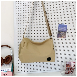 Detail of khaki nylon crossbody bucket bag with black logo on a white pegboard wall