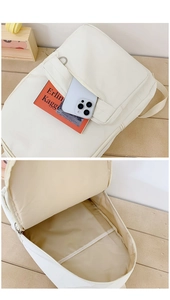 Detail of white minimalist canvas backpack showing large front pocket and inner storage layers