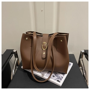 Detailed view of large brown tote bag featuring a golden oval metal buckle and long straps