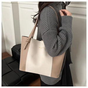 Side view of a large cream and khaki patchwork tote bag worn by a model in a minimalist room