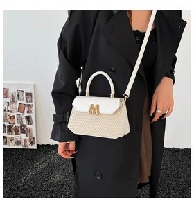 Détail d'un sac bandoulière tissé avec boucle métallique dorée et fine bandoulière blanche