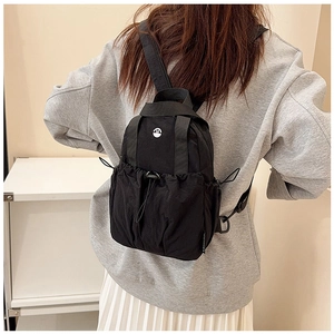 Detail of black mini drawstring backpack with white round M logo and nylon texture