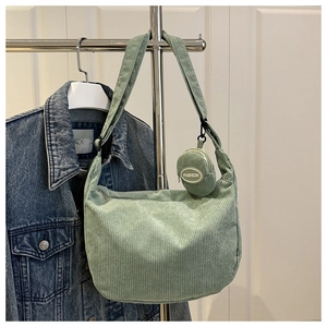 Detail of light green corduroy shoulder bag featuring a mini 'FASHION' charm on strap
