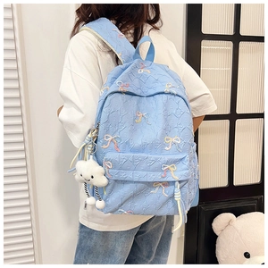 Detail view of light blue quilted backpack featuring colorful bow embroidery and cloud charm