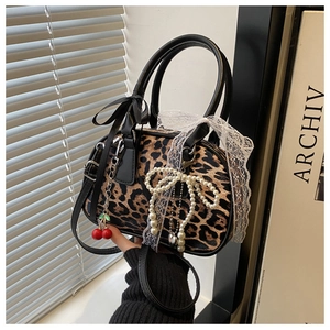 Detail of leopard print bag with lace bow, pearl charm, and red cherry pendant accessory