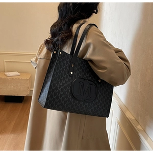 Close-up of black leather tote bag featuring M letter print and large embossed M logo