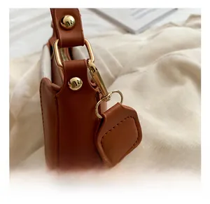 Detail of gold metal hook and cream woven strap on a brown fashion crossbody bag
