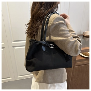 Detail view of black faux suede tote bag with leather strap on model in beige blazer