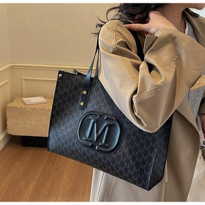 Detail of black tote bag featuring all-over M monogram pattern and gold rivet accents